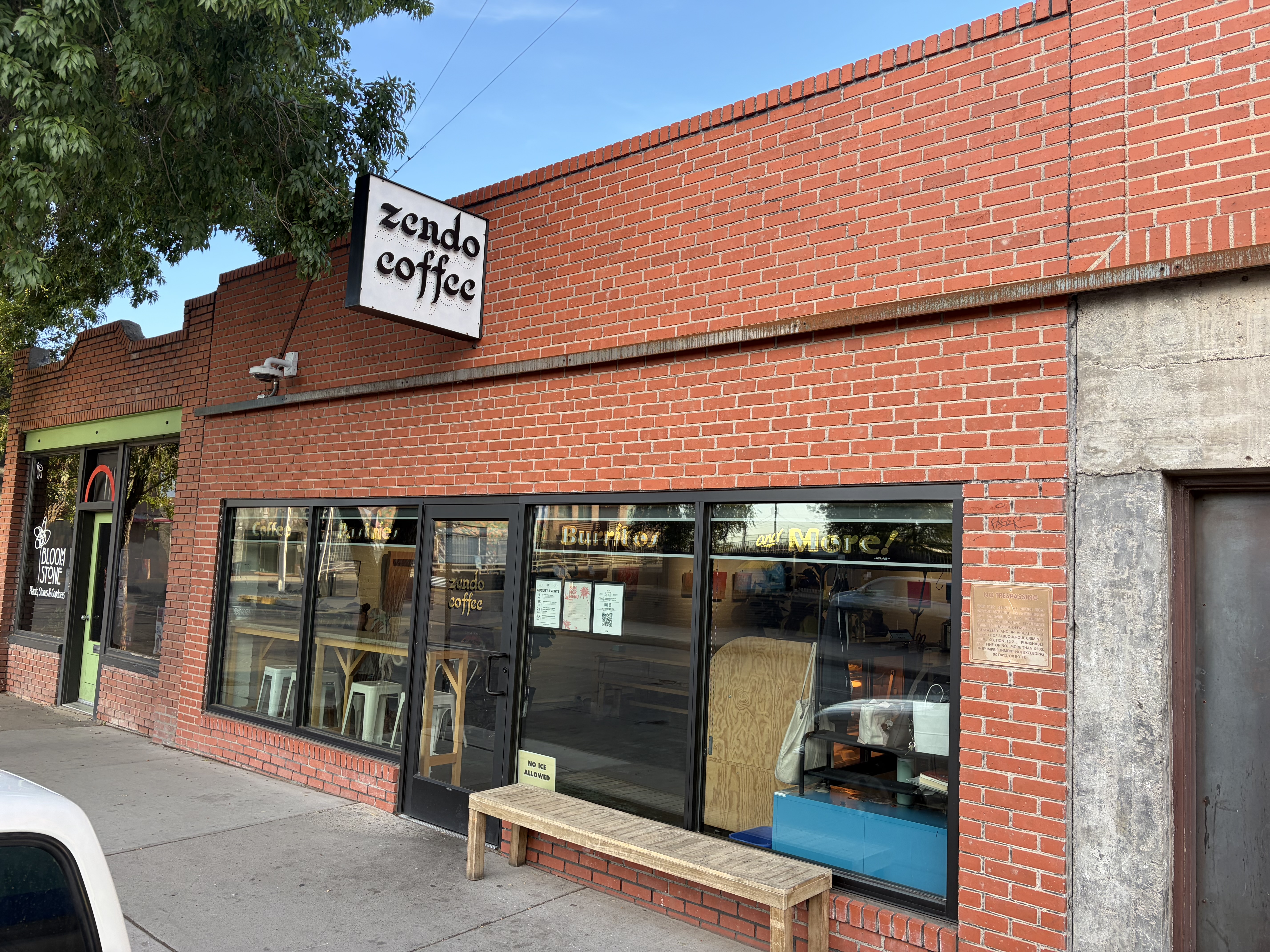 Zendo Coffee storefront: red brick, a hanging sign reading zendo coffee, tall windows and a wooden bench on the sidewalk.