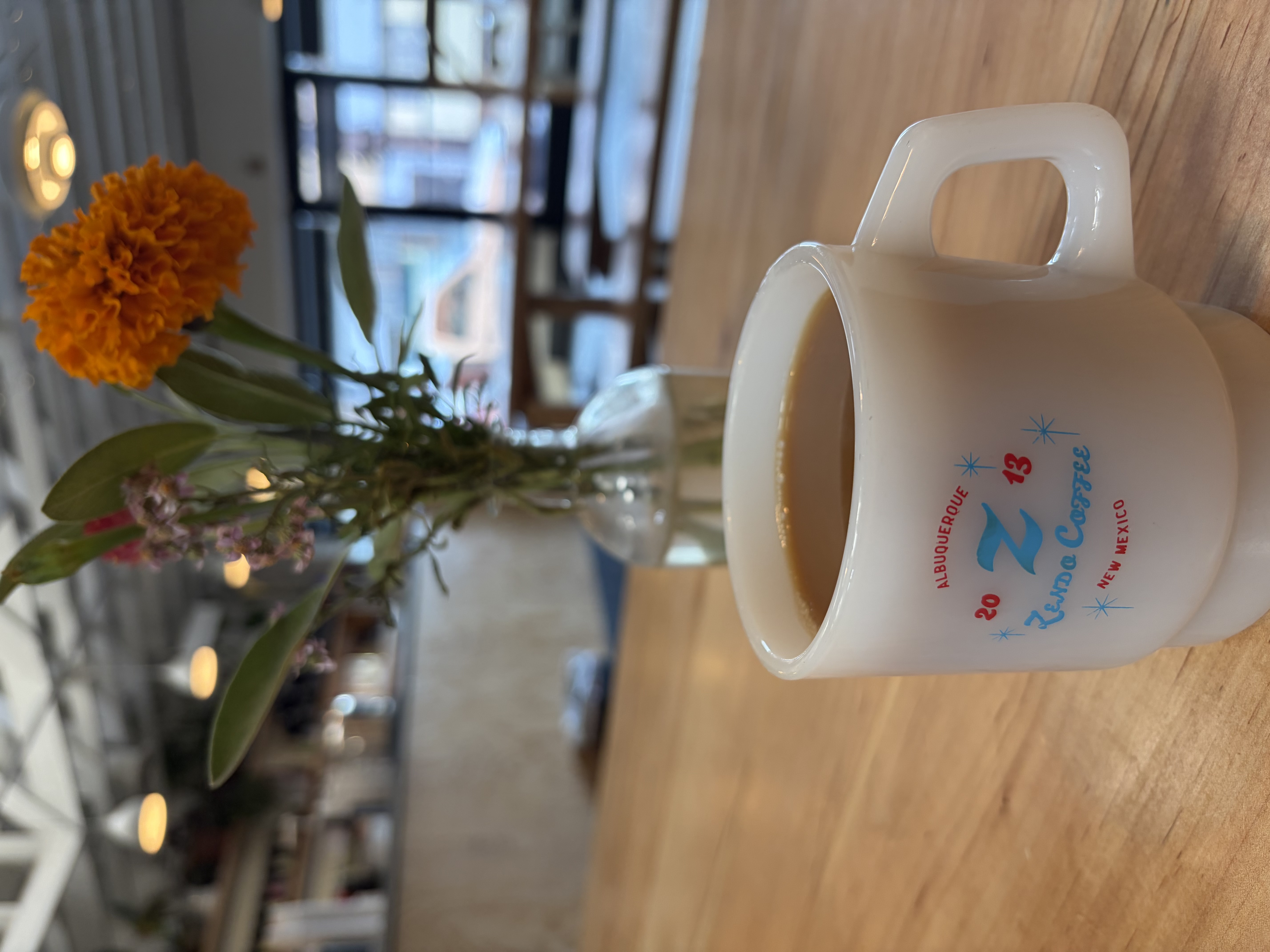 An Americano in a white Zendo Coffee mug printed with a Z, 2013, Albuquerque New Mexico, beside a marigold in a glass vase.